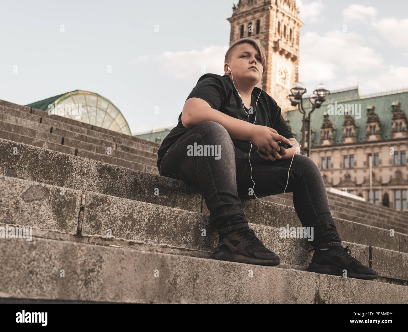 Ein junger Mann mit Ohrhörer sitzt auf Schritte Stockfoto