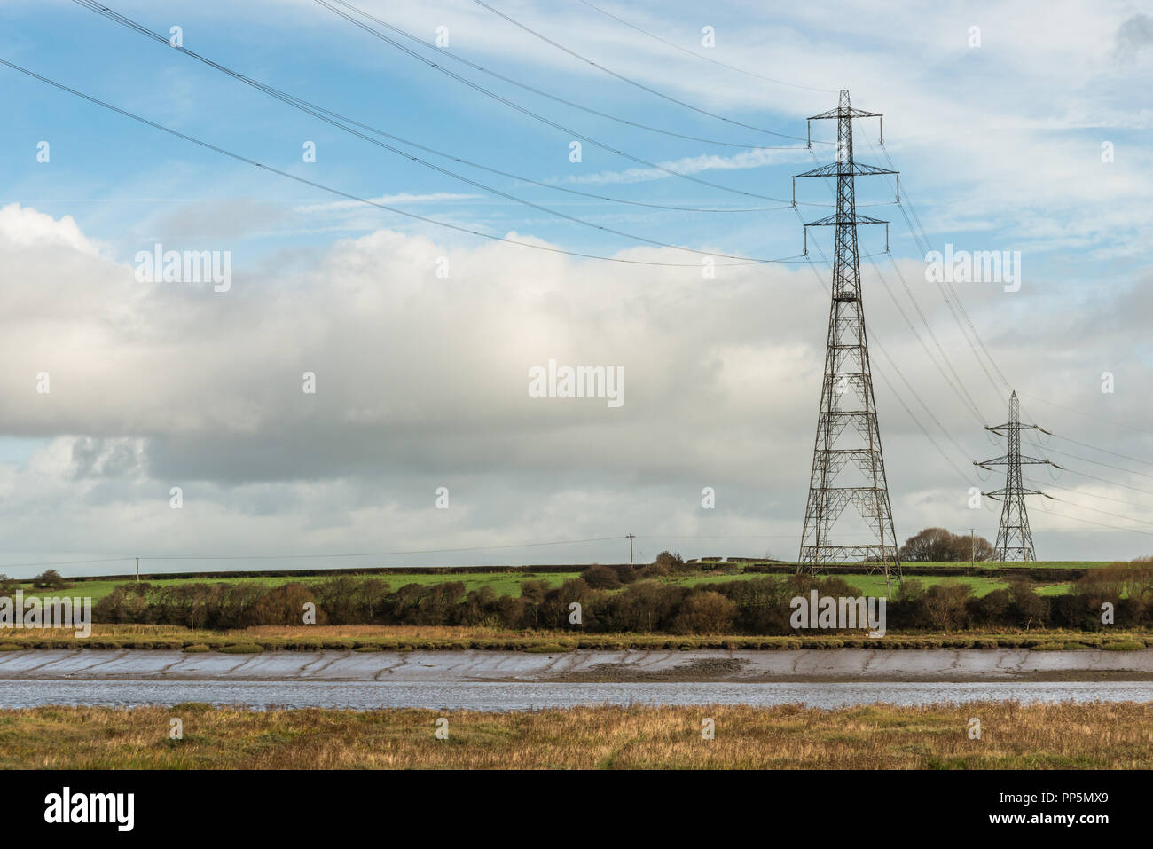 Zwei Masten auf der Seite des Flusses Wyre in Lancashire, England, Großbritannien mit Hochspannungskabeln Kreuzung das Wasser in der Landschaft. Stockfoto