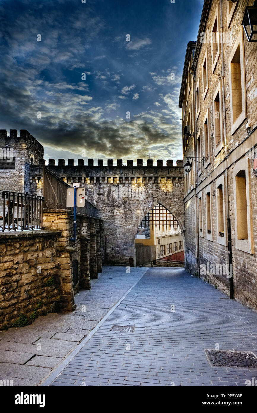 High Dynamic Range Foto von eine Straße in der Altstadt von Vitoria, Spanien, mit Teil einer mit Zinnen versehene Wand und ihre Geharkt, Tür, gepflasterten Boden und Granit Stein Fassaden Stockfoto