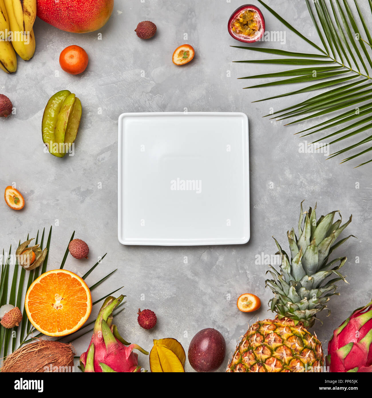 Quadratische weiße leere Platte nalmium Blätter und Früchte, saftig Trio kumkva, Physalis, Passionsfrucht, Banane auf grauem Beton Hintergrund mit kopieren. Die Zusammensetzung von Lebensmitteln. Flach Stockfoto