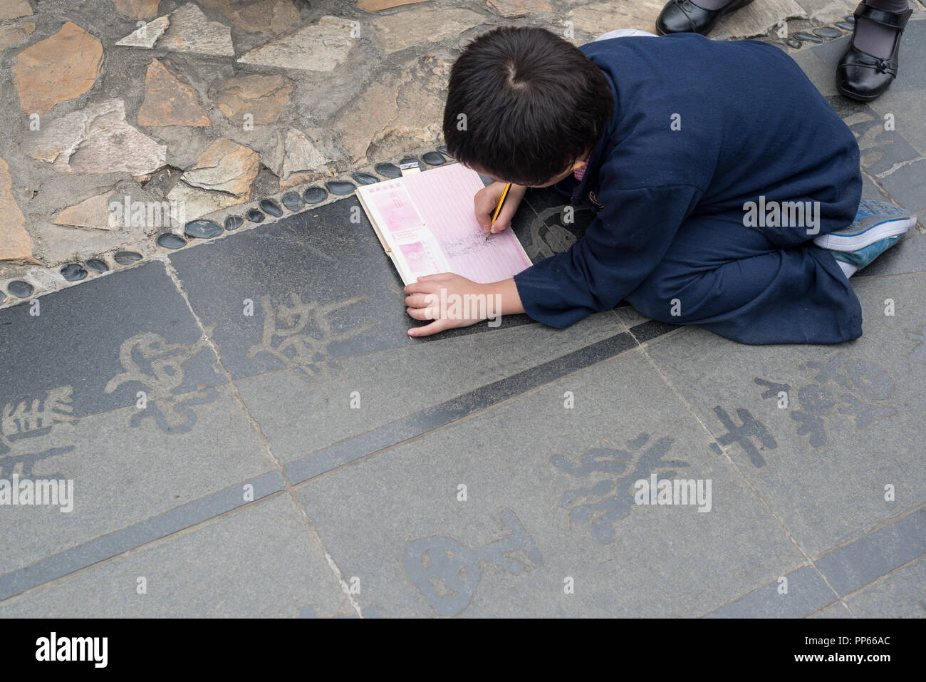 Chengdu, Provinz Sichuan, China - Okt 2nd, 2017: Kleiner Junge Kopieren der chinesischen Poesie in einem Lehrbuch auf dem Boden in HuanHuanXi öffentlichen Park Stockfoto
