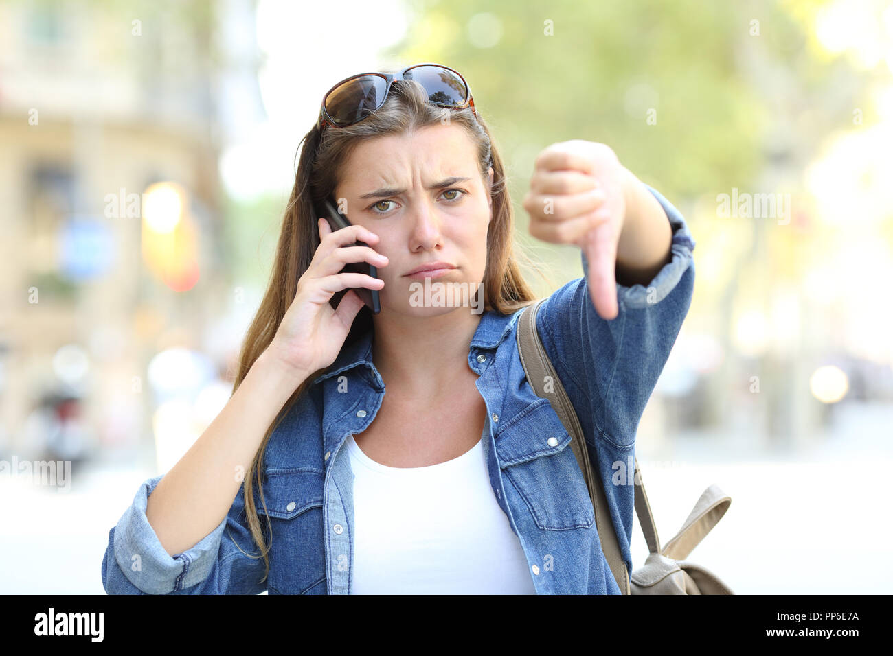 Vorderansicht Porträt eines zornigen Mädchen am Telefon sprechen mit Daumen nach unten auf der Straße Stockfoto