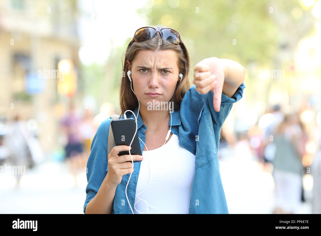 Vorderansicht Portrait von einem genervten Mädchen, das Hören von Musik mit Daumen nach unten auf der Straße Stockfoto