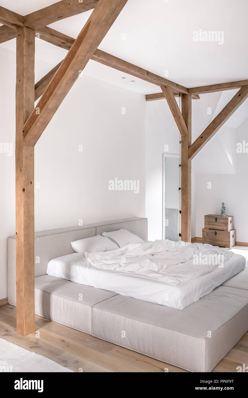 Modernes Schlafzimmer mit weißen Wänden, Holzbalken und Parkettboden mit  Teppichen auf dem Boden. Es ist ein grauer Bett mit Licht Handtücher,  Truhen mit einer Statuette Stockfotografie - Alamy