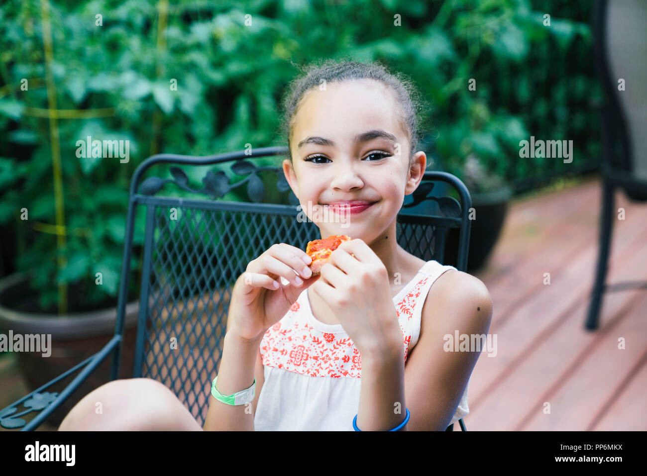 Lächelnde Mädchen essen Pizza im Hinterhof auf der Veranda Stockfoto