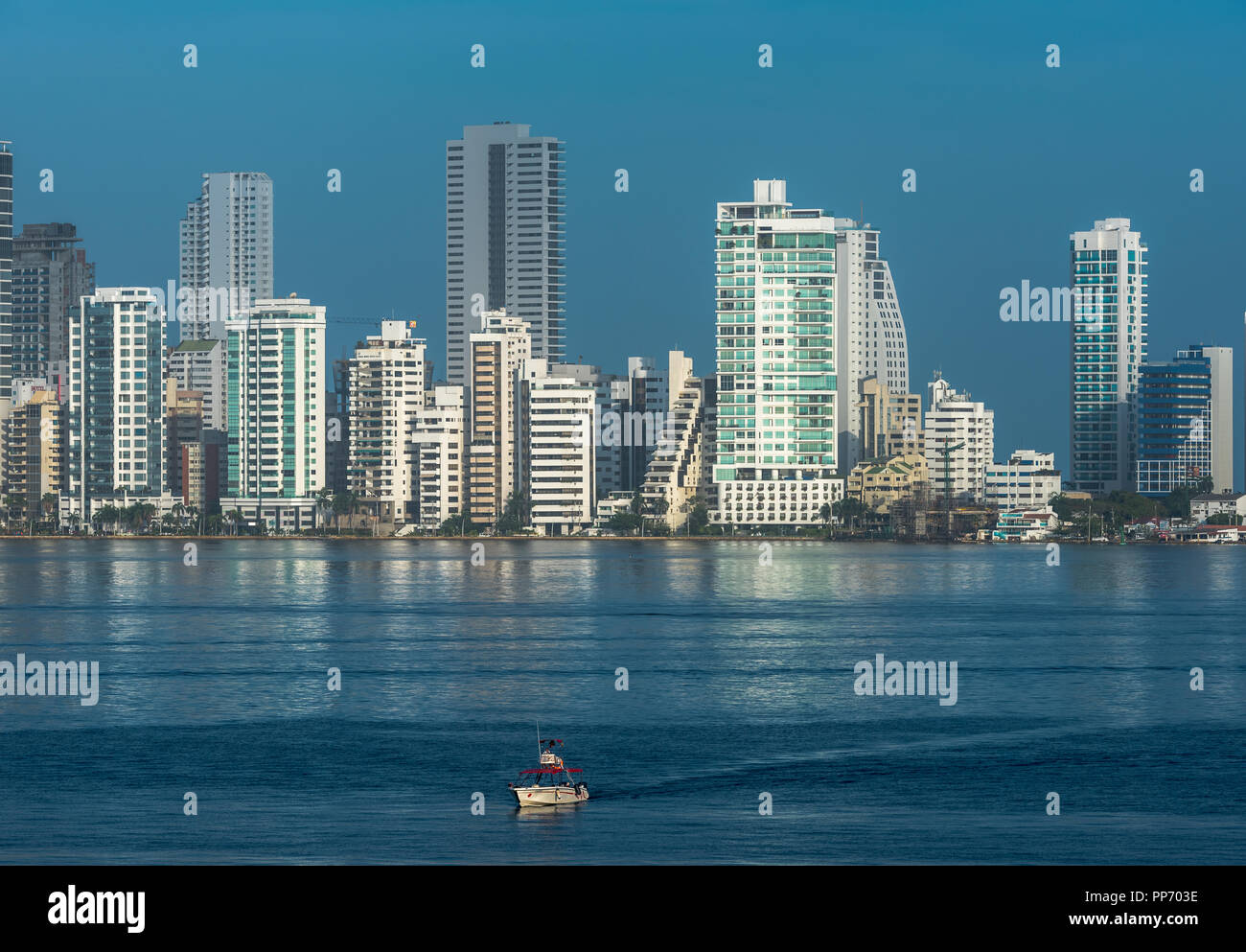 Ein kleines Boot segelt auf dem blauen Wasser der Bucht von Cartagena mit Wolkenkratzer der Stadt in den Hintergrund. Stockfoto