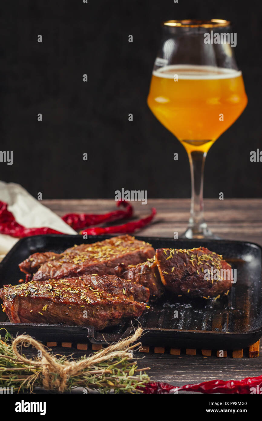 Gegrilltes Fleisch Steaks auf der Pfanne und ein Glas Bier auf dunklem Hintergrund Stockfoto