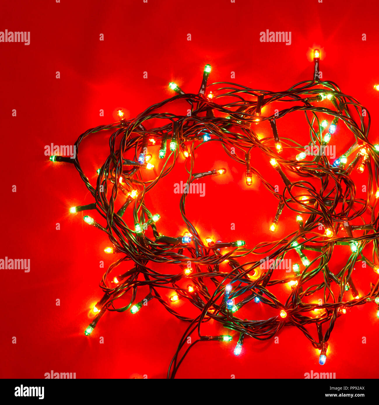 Weihnachtsbeleuchtung in verschiedenen Farben auf rotem Hintergrund Stockfoto