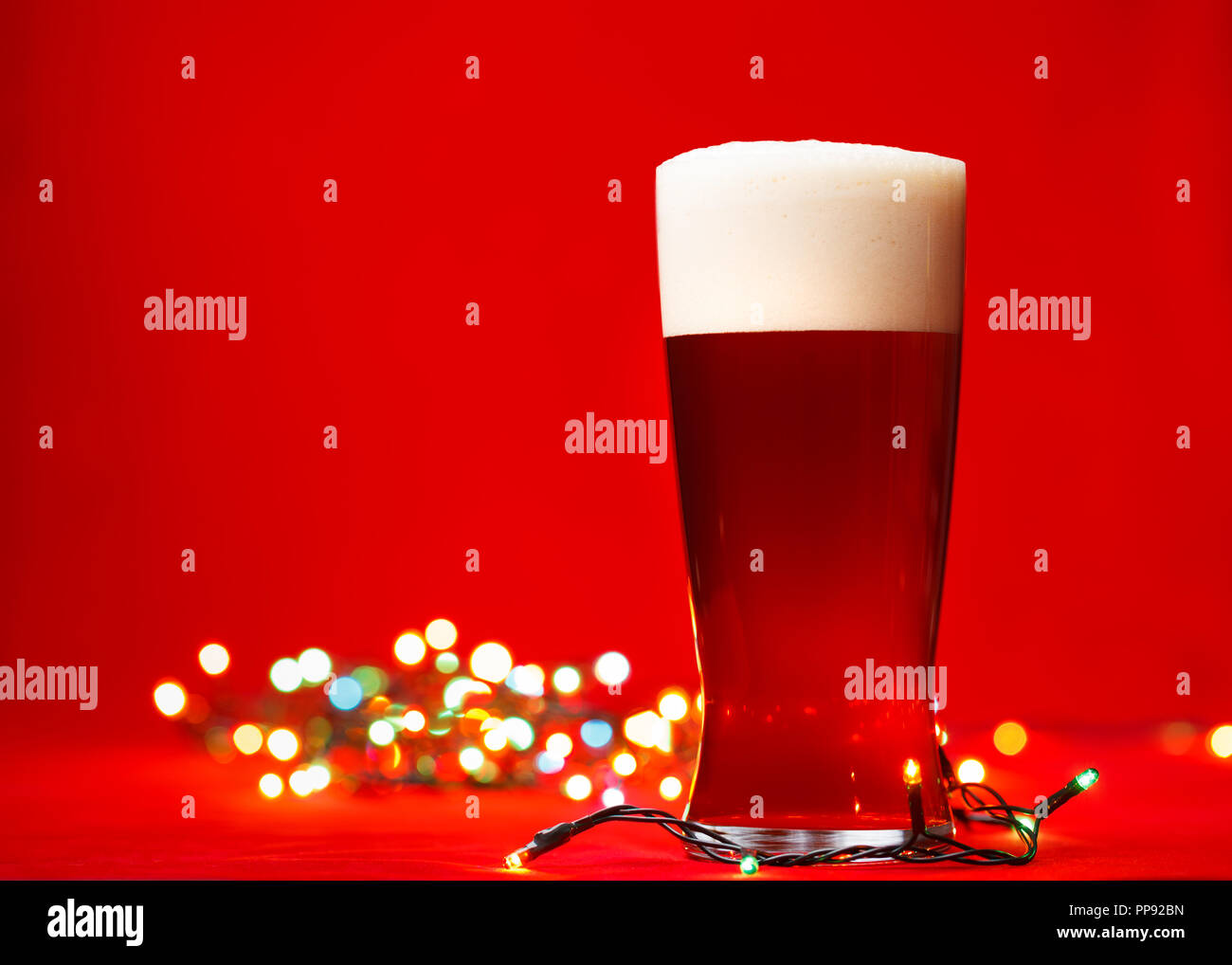 Glas Bär oder Ale mit Weihnachtsbeleuchtung auf rotem Hintergrund Stockfoto