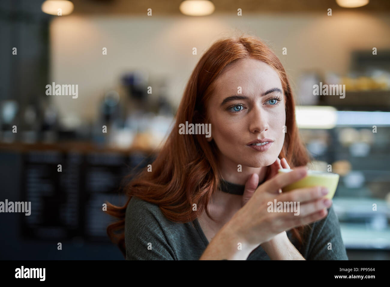 Eine einzelne Frau, sitzt in einem City Cafe mit einem heißen Getränk in einem Becher, nachdenklich, der Blick in die Ferne Stockfoto
