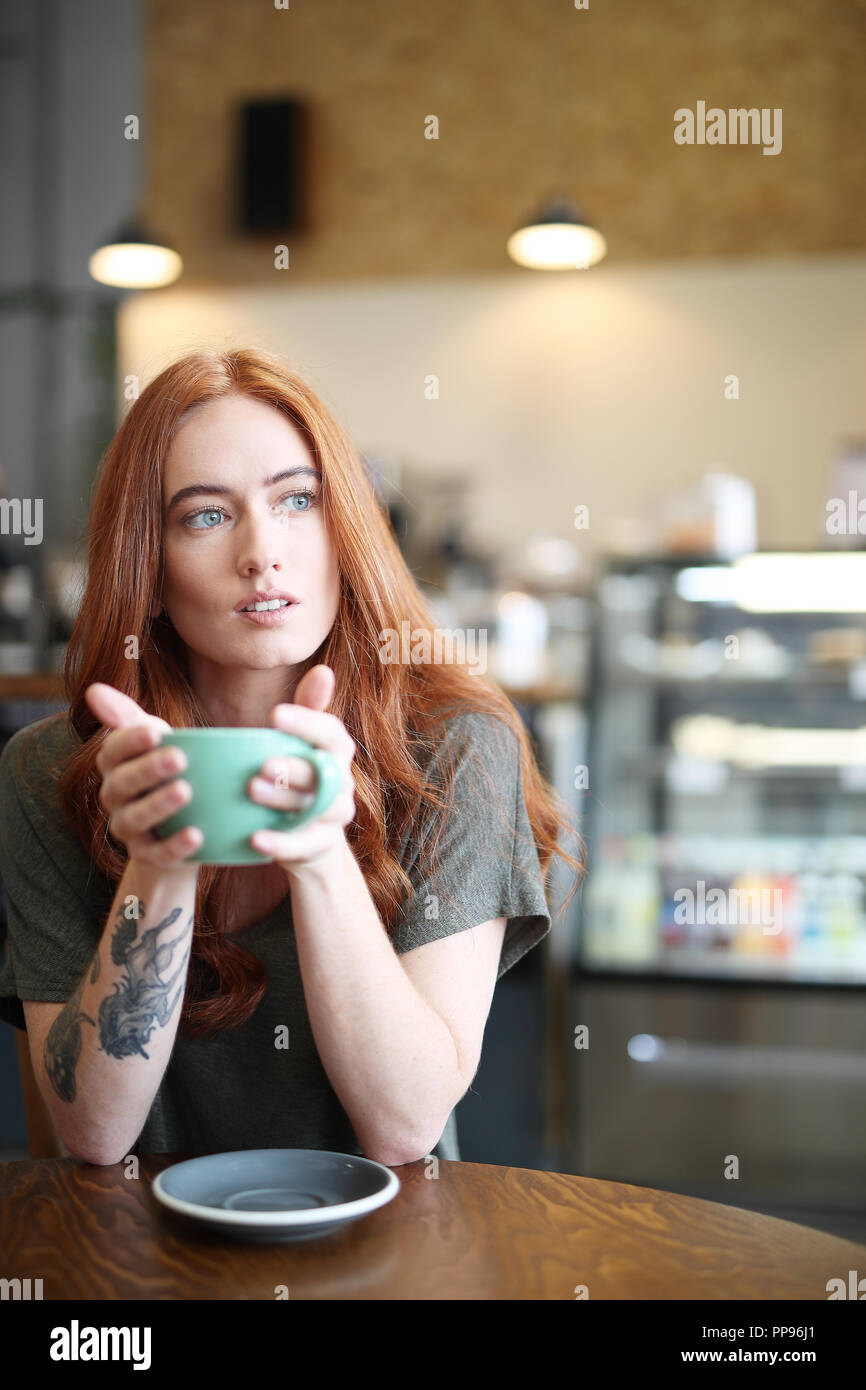 Redhead, weiblicher Single, sitzt in einem City Cafe mit einem heißen Getränk in einer Schale. Stockfoto