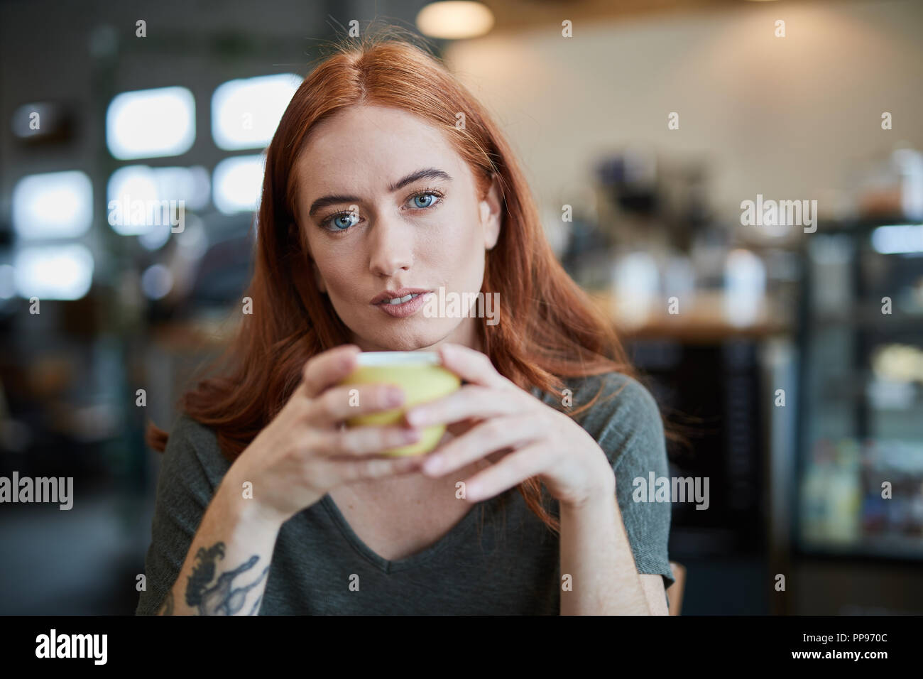 Eine einzelne Frau, sitzt in einem City Cafe mit einem heißen Getränk in einem Becher, an Kamera suchen Stockfoto