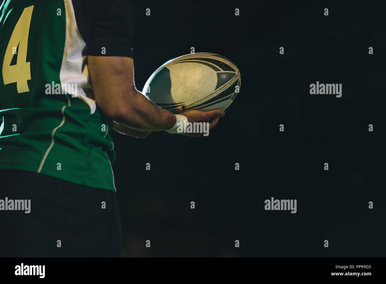 Abgeschnittener Schuss eines professionellen Rugbyspielers in Uniform, der im Nachtspiel einen Ball hält. rugby-Spieler mit Ball in der Hand. Stockfoto