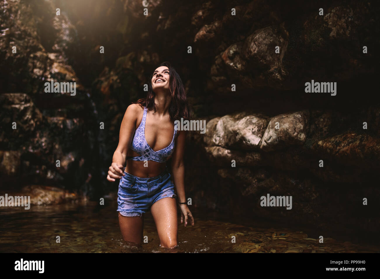 Junge kaukasier schöne Frau Tourist in einen Wasserfall, Teich im Dschungel suchen und lächelnd. Schöne Mädchen mit Bikini Top und Shorts im Teich Stockfoto