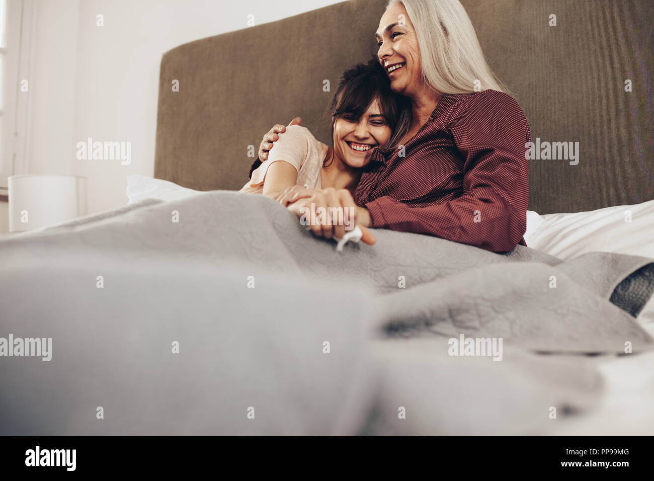 Ältere Frau, die ihre Tochter in den Arm beim Sitzen auf dem Bett. Mutter und Tochter die Zeit gemeinsam zu Hause. Stockfoto