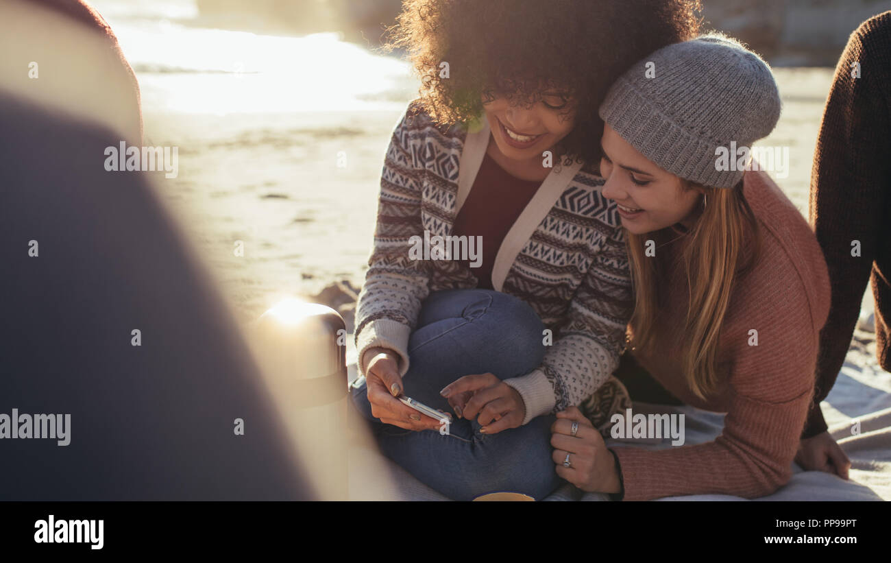 Junge Freunde genießen eine Beach Party mit Handy und lächelnd. Zwei junge Frau auf der Suche etwas lustig auf dem Smartphone und lächelnd. Stockfoto