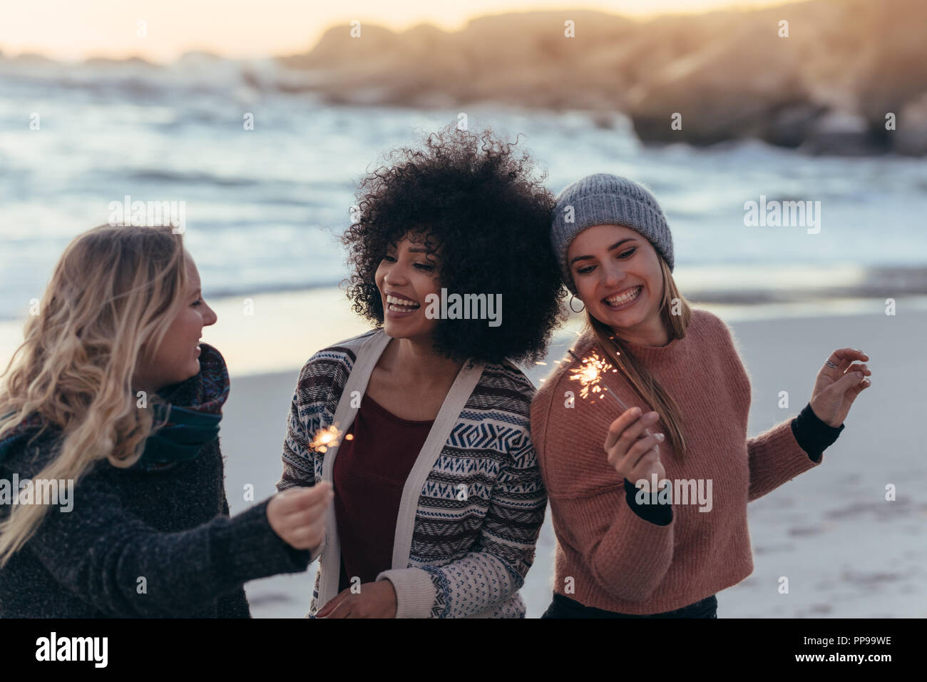 Gerne Freunde feiern am Strand mit Wunderkerzen. Vielfältige Gruppe von Frau Freunde zusammen am Strand feiert Tag des neuen Jahres am Strand. Stockfoto