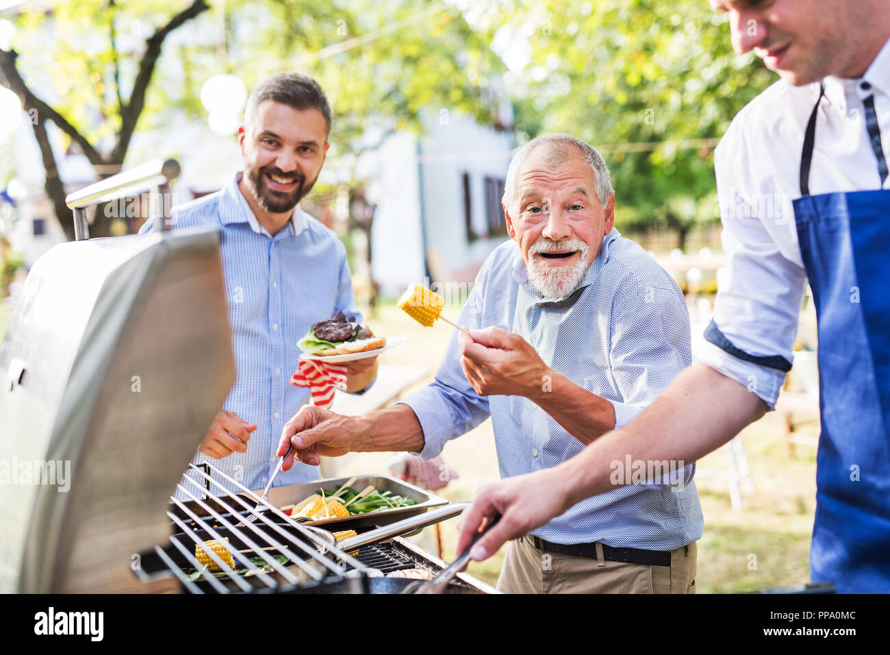 Männer mit Familie und Freunden kochen auf einer Grillparty. Stockfoto