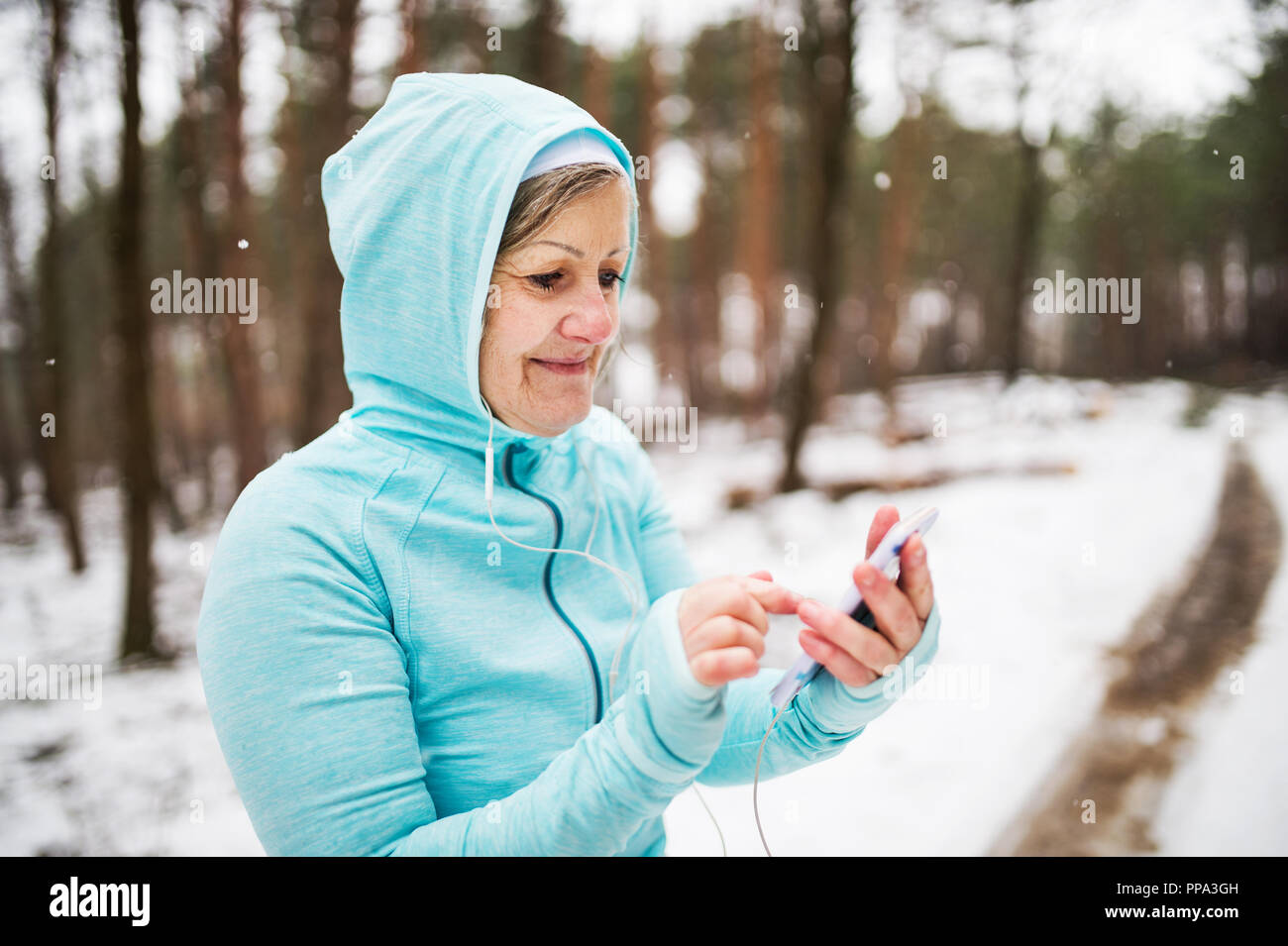Ältere Frau Runner mit Smartphone im Winter Natur, Ruhe. Stockfoto