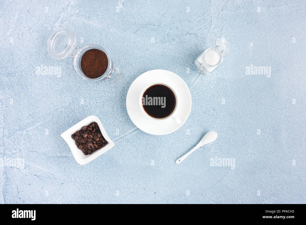 Stillleben mit schwarzen Kaffee in der Tasse, Kaffeebohnen, gemahlenen Kaffee und Weißzucker auf Blau konkreten Hintergrund. Stockfoto