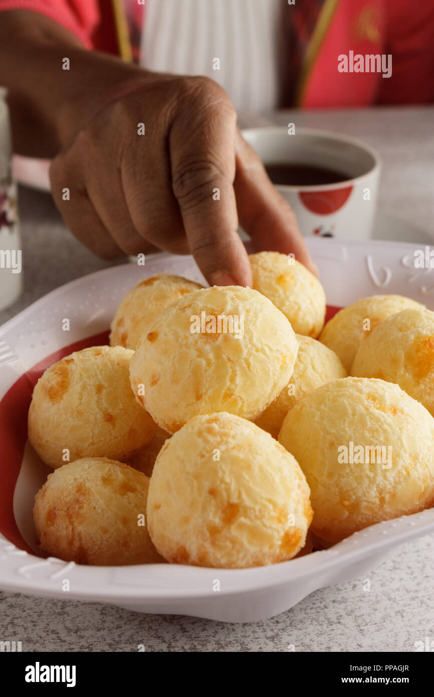 Eine weibliche Hand, denn ein Käse, Brot (auch bekannt als Pao De Queijo) aus dem Korb; typisch brasilianisches Frühstück Szene. Selektive konzentrieren. Stockfoto