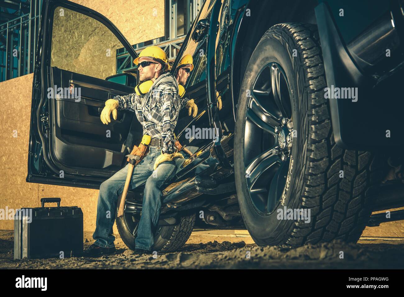 Kaukasische Baugewerbe Arbeiter in seinem 30s Entspannen nach einem harten Arbeitstag. Arbeitnehmer und seine schwarzen Pickup Truck. Industrielle Thema. Stockfoto