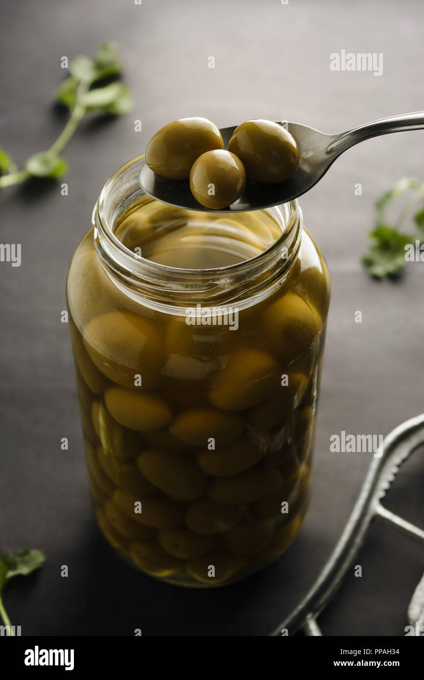 Plongée Blick auf saftig grüne Oliven aus dem Glas auf einem silbernen Löffel genommen zu werden. Schwarzer Hintergrund, selektiven Fokus. Stockfoto