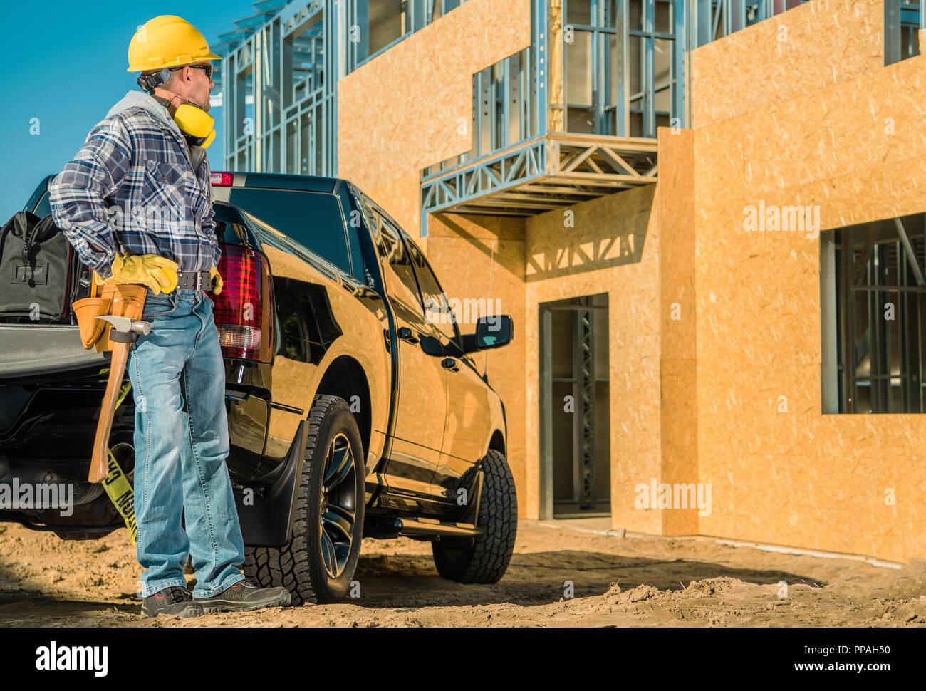 Wohn- Baustelle. Junge kaukasier Auftragnehmer Arbeiter in seinem 30s und seinem Pickup Truck vor der neu errichteten Gebäude. Metal Frame a Stockfoto