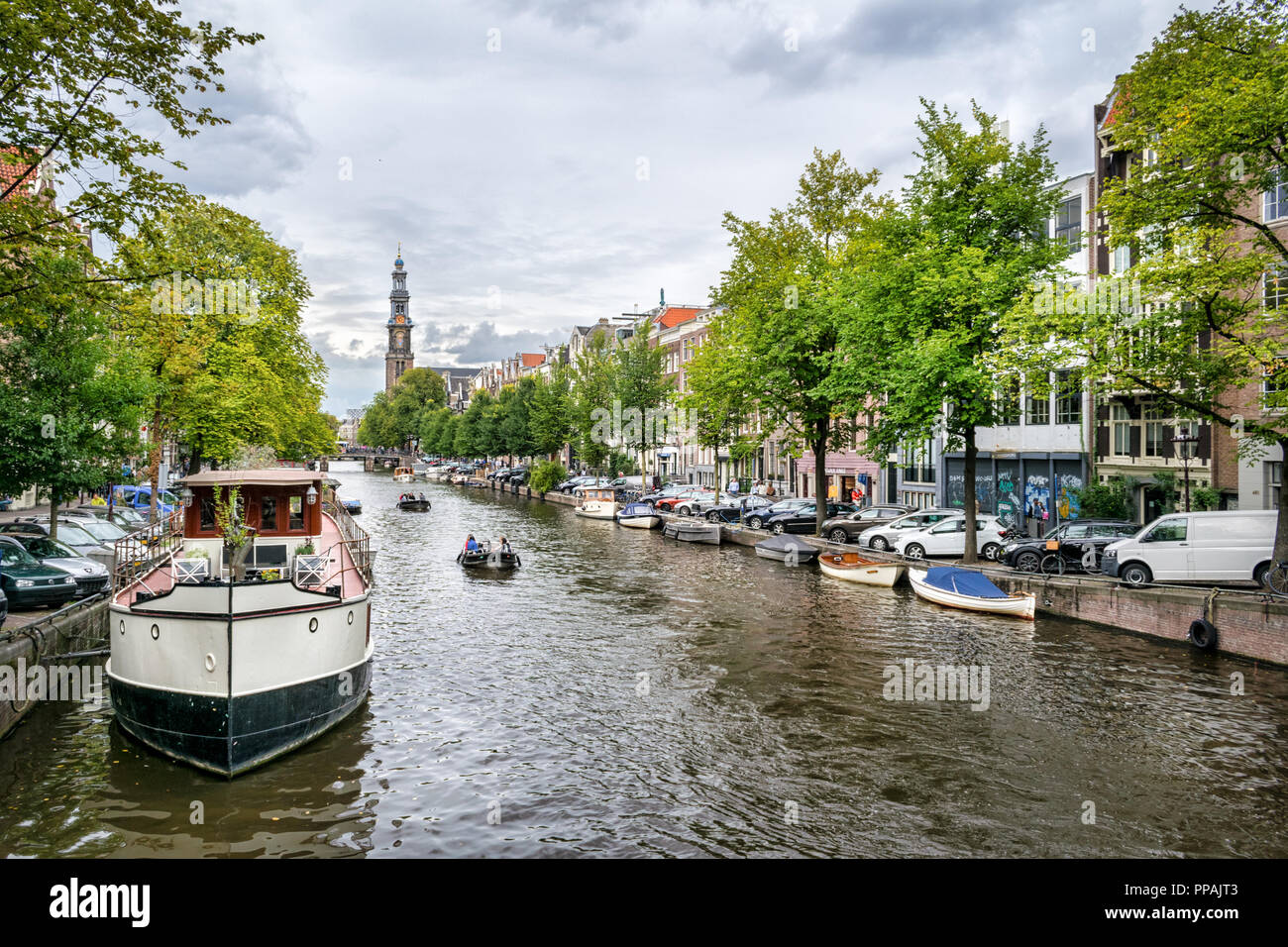 Das ist ein Bild von einer der vielen Grachten Amsterdams. Es gibt einen Großen Kanal Boot im Vordergrund und eine Kirche im Hintergrund Stockfoto