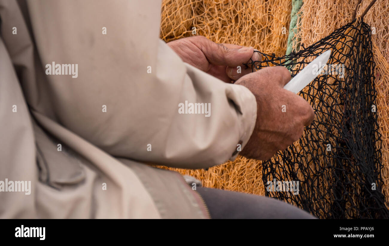 Die Hände eines Fischers Instandsetzung ein fischernetz mit einem Messer. Stockfoto