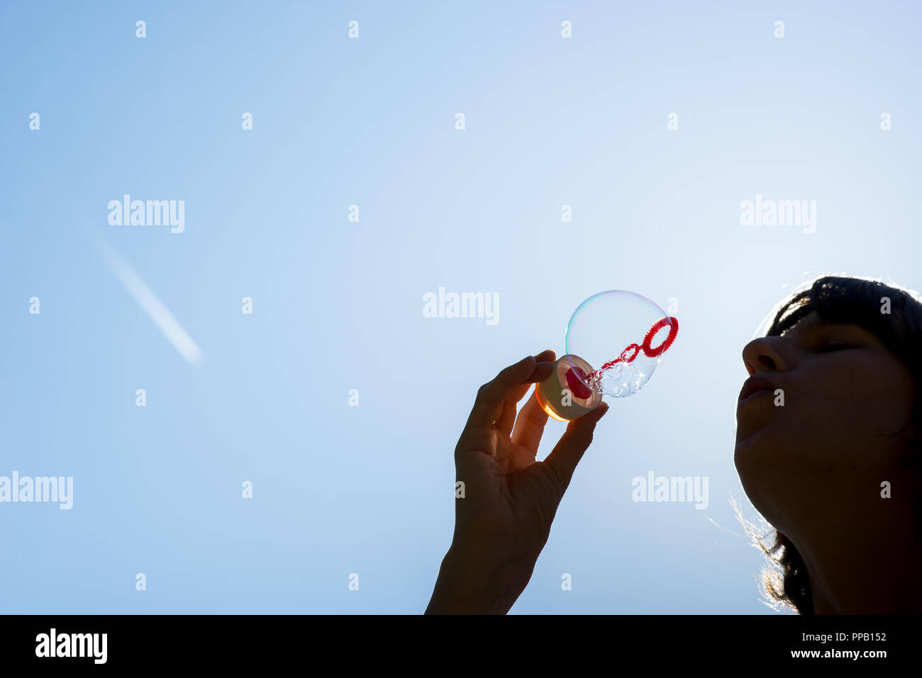 Low Angle Nahaufnahme der Silhouette einer Frau bläst Seifenblasen gegen einen sonnigen blauen Himmel mit viel copyspace in einem konzeptionellen Bild. Stockfoto