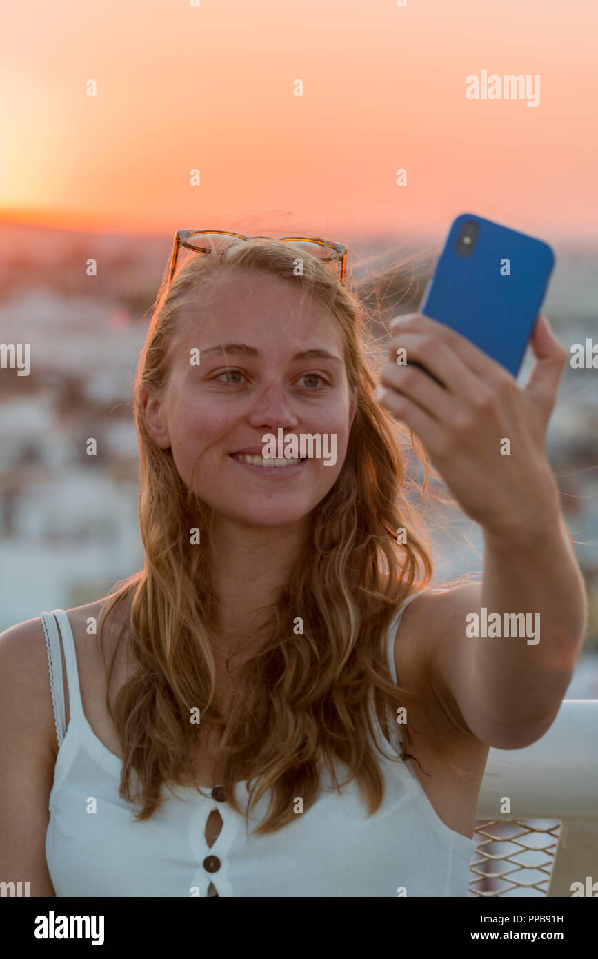 Junge Frau mit Weiß top Fotos selbst mit einem Smartphone, einem selfie, Sonnenuntergang, Plaza de la Encarnacion, Sevilla, Andalusien Stockfoto