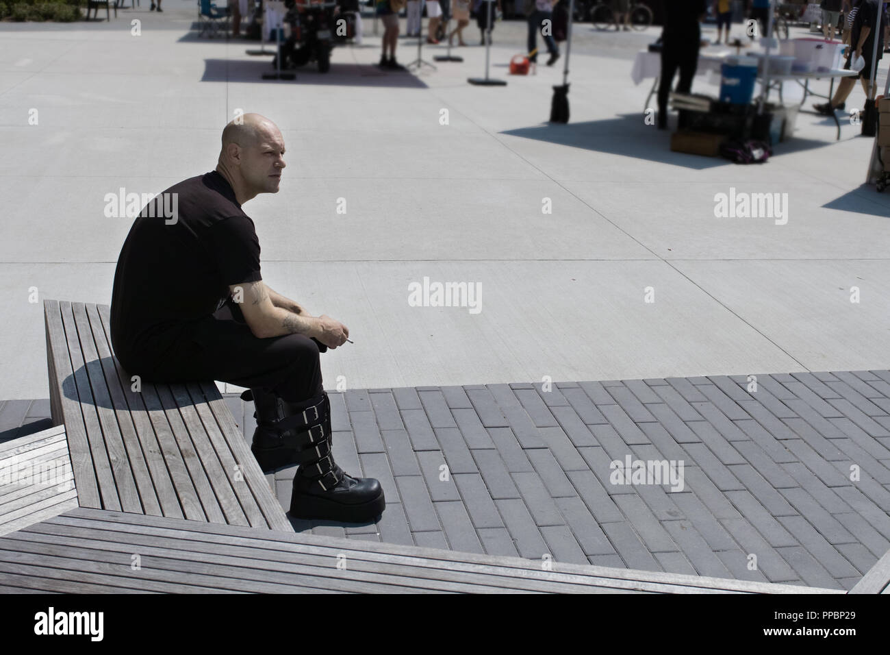Junger Mann Gothic gekleidet, Sitzen und smocking eine Zigarette auf dem Platz Markt in Stratford, Ontario. Stockfoto