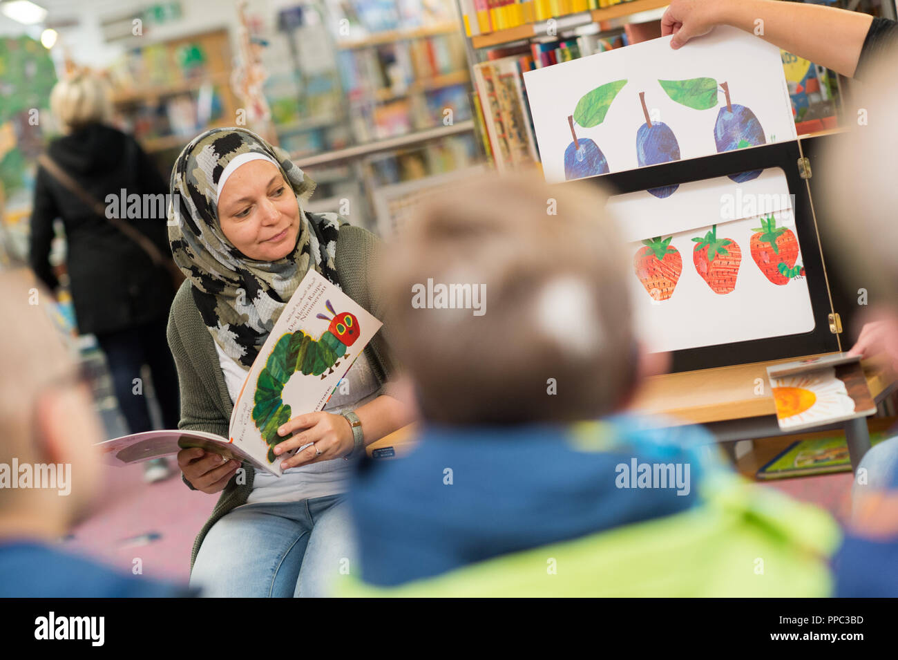 25. September 2018, Sachsen-Anhalt, Bernburg: Shirin Alabid liest die Geschichte "Die kleine Raupe Nimmersatt" auf Arabisch zu einer Gruppe von Kindergartenkindern. Im Rahmen des Projekts "Willkommen in Meine Bibliothek - Vielfalt und Mehrsprachigkeit in der Bibo und Kita', der bernburger Stadtbibliothek erhielt eine Vielfalt der Groß- und Kleinschreibung, mehrsprachige Medien Sammlung an Kinder mit Migrationshintergrund ausgerichtet. Foto: Klaus-Dietmar Gabbert/dpa-Zentralbild/ZB Stockfoto