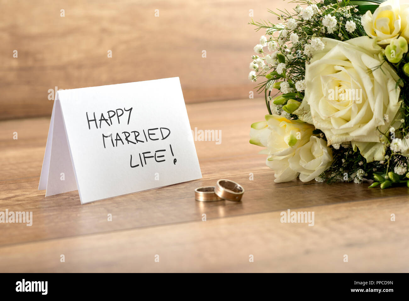 In der Nähe von wunderschönen Braut Strauß mit frischen Blumen, ein Paar Ringe und glückliches Eheleben Karte für Brautpaare auf Holztisch. Stockfoto