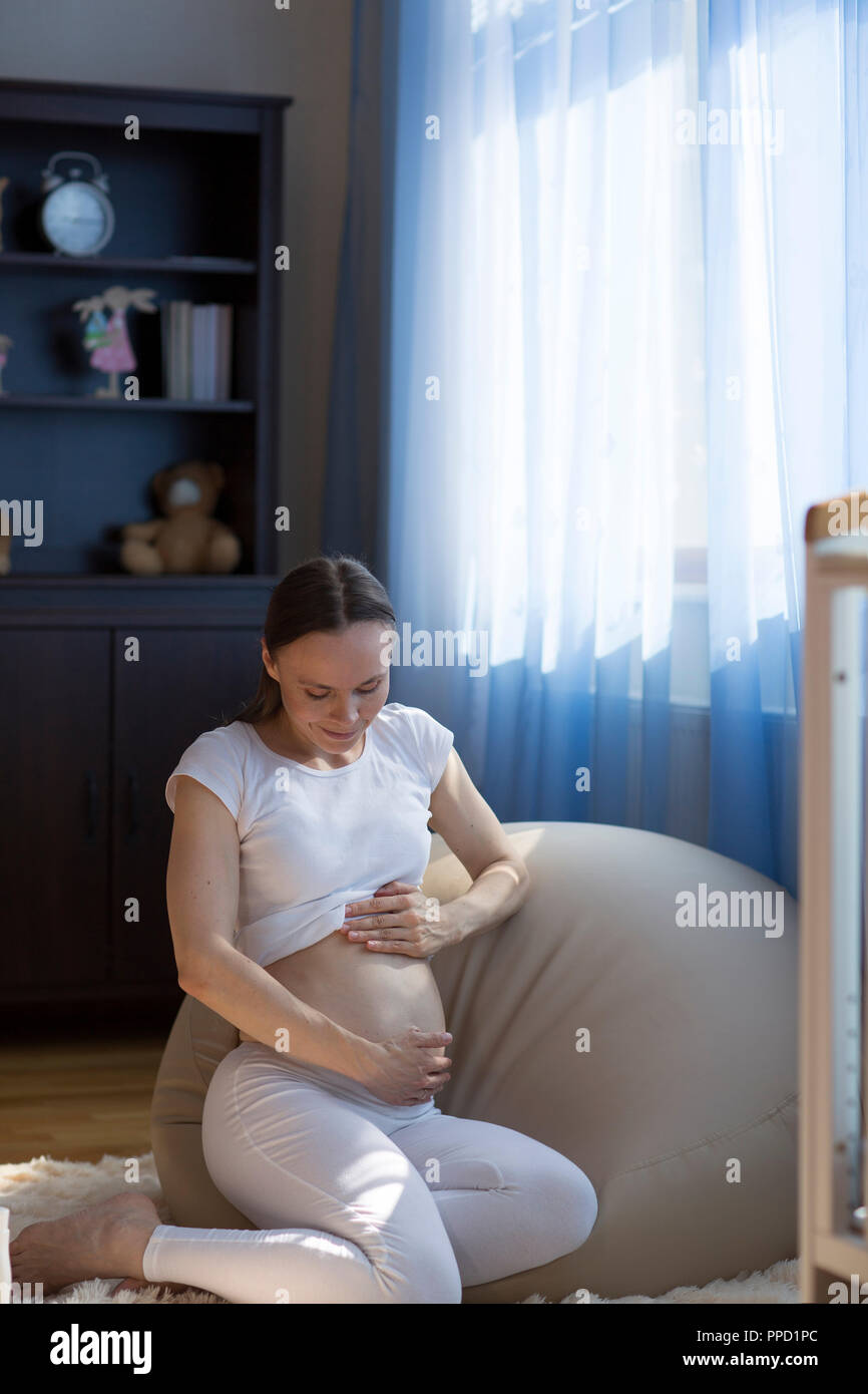 Junge schwangere Frau zwischen 30 und 35 Jahre alt, liebkost ihre ihren Bauch Stockfotografie ...