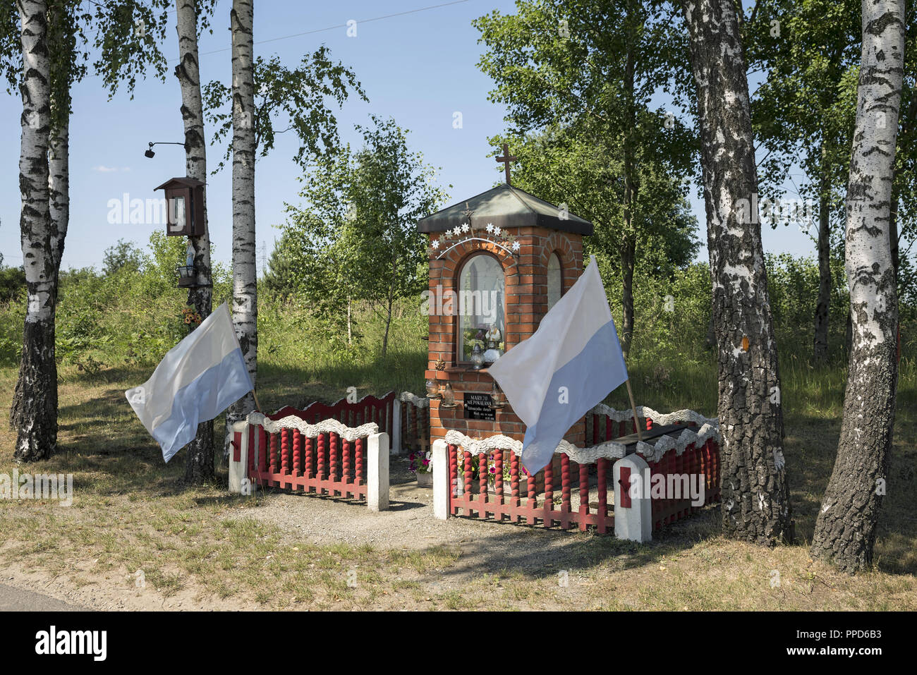 Eine kleine Kapelle unter Birken gebaut von Backstein und eingezäunt mit einem konkreten Zaun mit einer Abbildung der Jungfrau Maria, die Unbefleckte, Ostrzeszów, Polen Stockfoto
