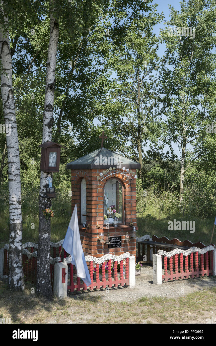 Eine kleine Kapelle unter Birken gebaut von Backstein und eingezäunt mit einem konkreten Zaun mit einer Abbildung der Jungfrau Maria, die Unbefleckte, Ostrzeszów, Polen Stockfoto