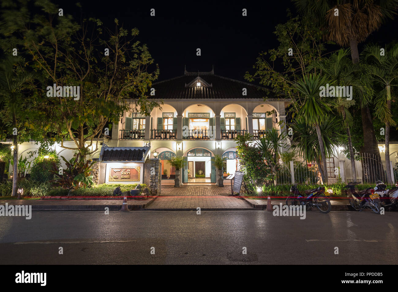 Paar Roller vor der beleuchteten Villa Santi, ein Hotel in einer alten französischen Kolonialzeit Gebäude auf einer idyllischen Sakkaline Straße in Luang Prabang, Laos, in der Dämmerung. Stockfoto
