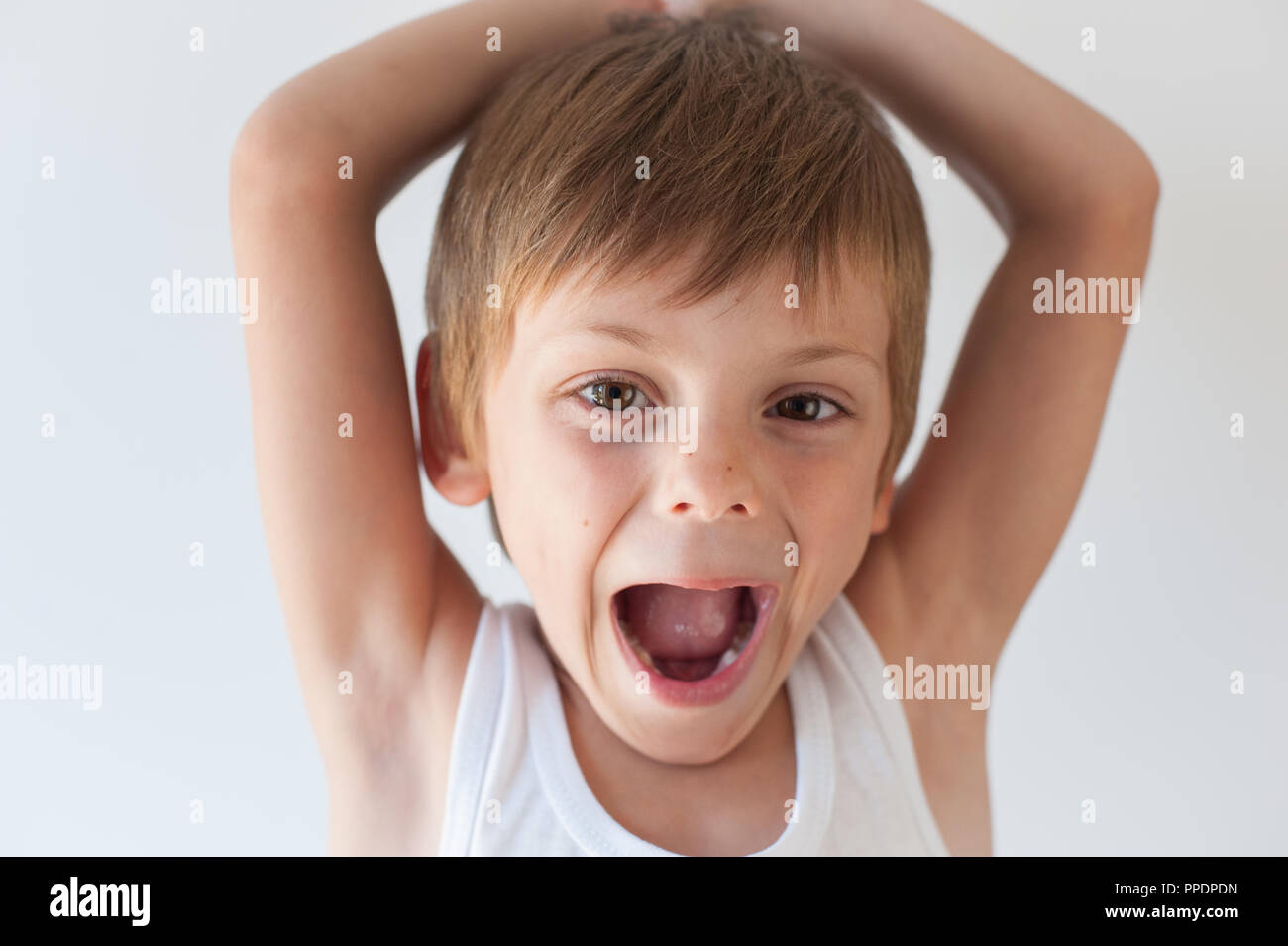 Gerne schreien wenig kaukasischen Jungen im weißen Hemd mit den Händen hinter seinem Kopf Stockfoto