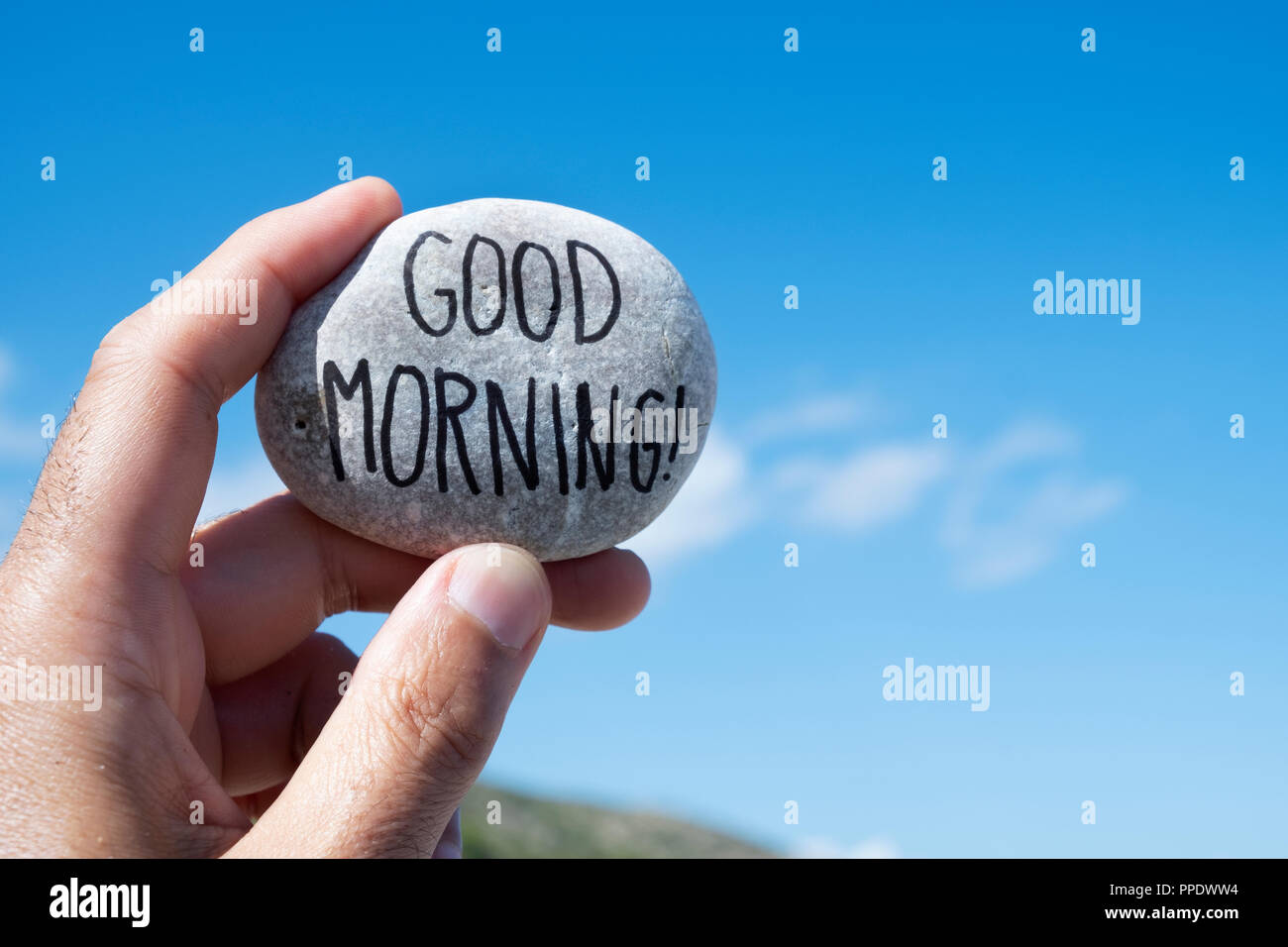 Nahaufnahme eines jungen kaukasischen Mann mit einem Stein mit dem Text guten Morgen geschrieben, indem sie gegen den blauen Himmel Stockfoto