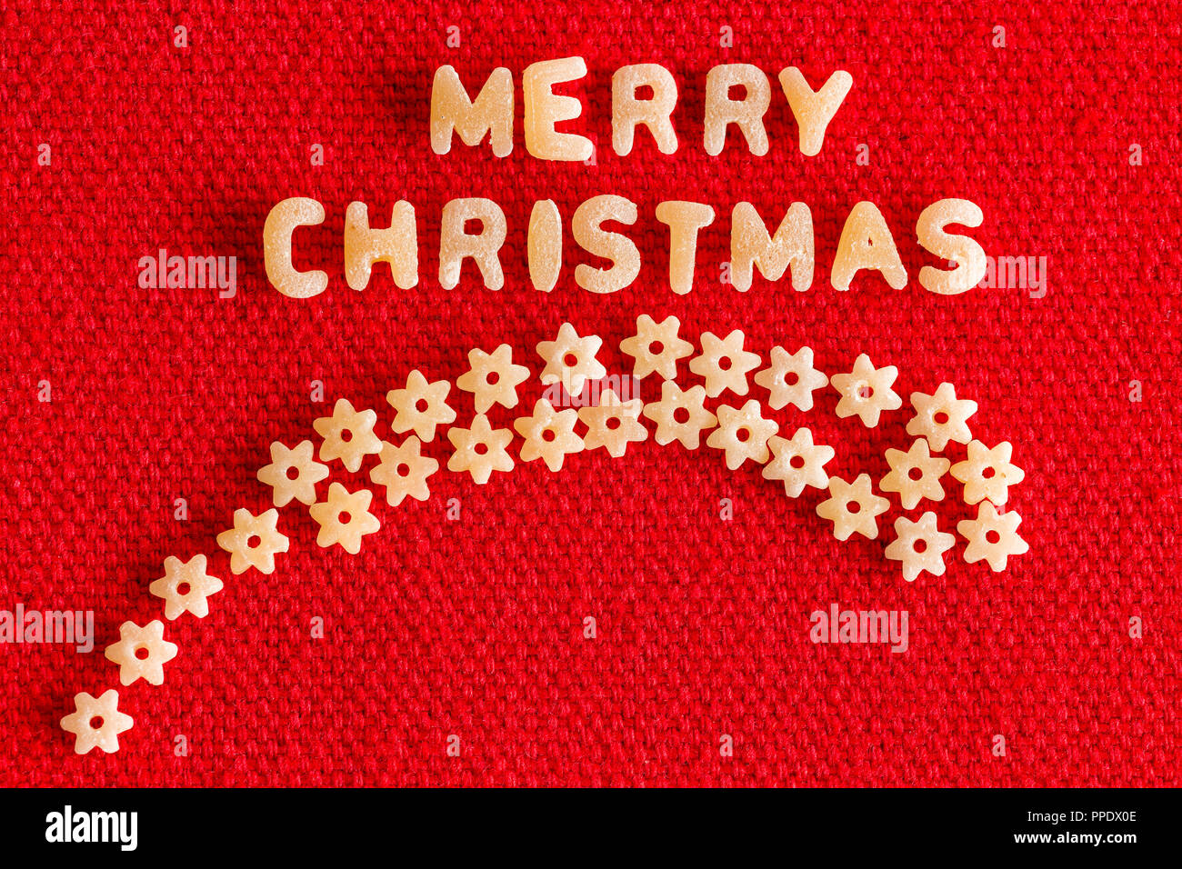 Alphabet geformte Teigwaren Buchstaben Rechtschreibung frohe Weihnachten und plain star Pasta wie Comet über hellen roten Hintergrund geformt Stockfoto
