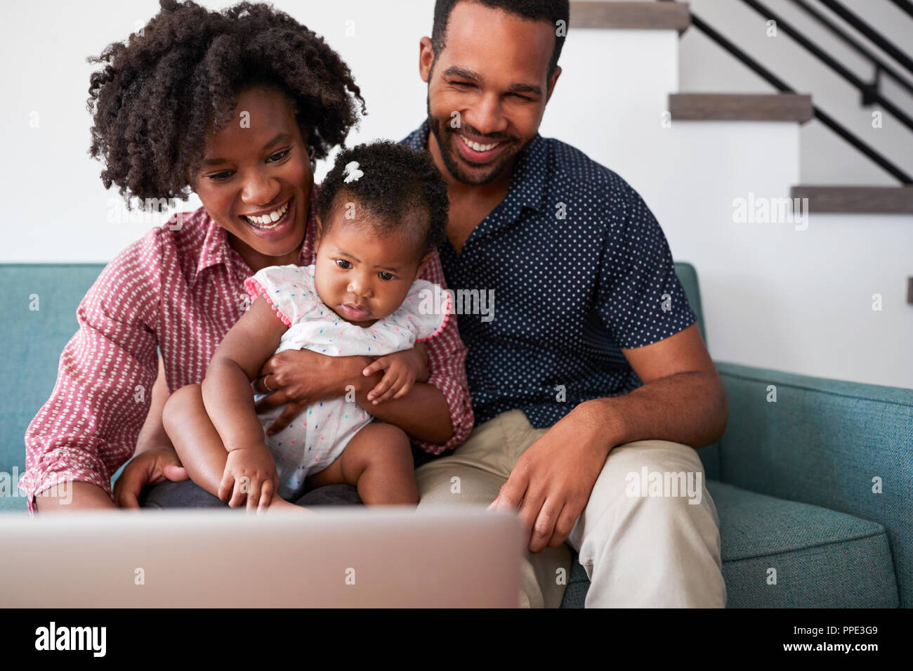 Familie mit Baby Tochter sitzt auf einem Sofa zu Hause auf Laptop Stockfoto