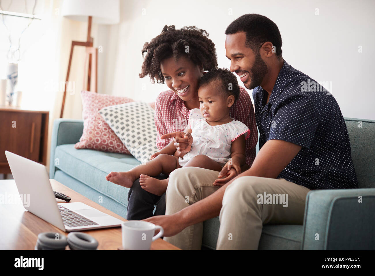 Familie mit Baby Tochter sitzt auf einem Sofa zu Hause auf Laptop Stockfoto