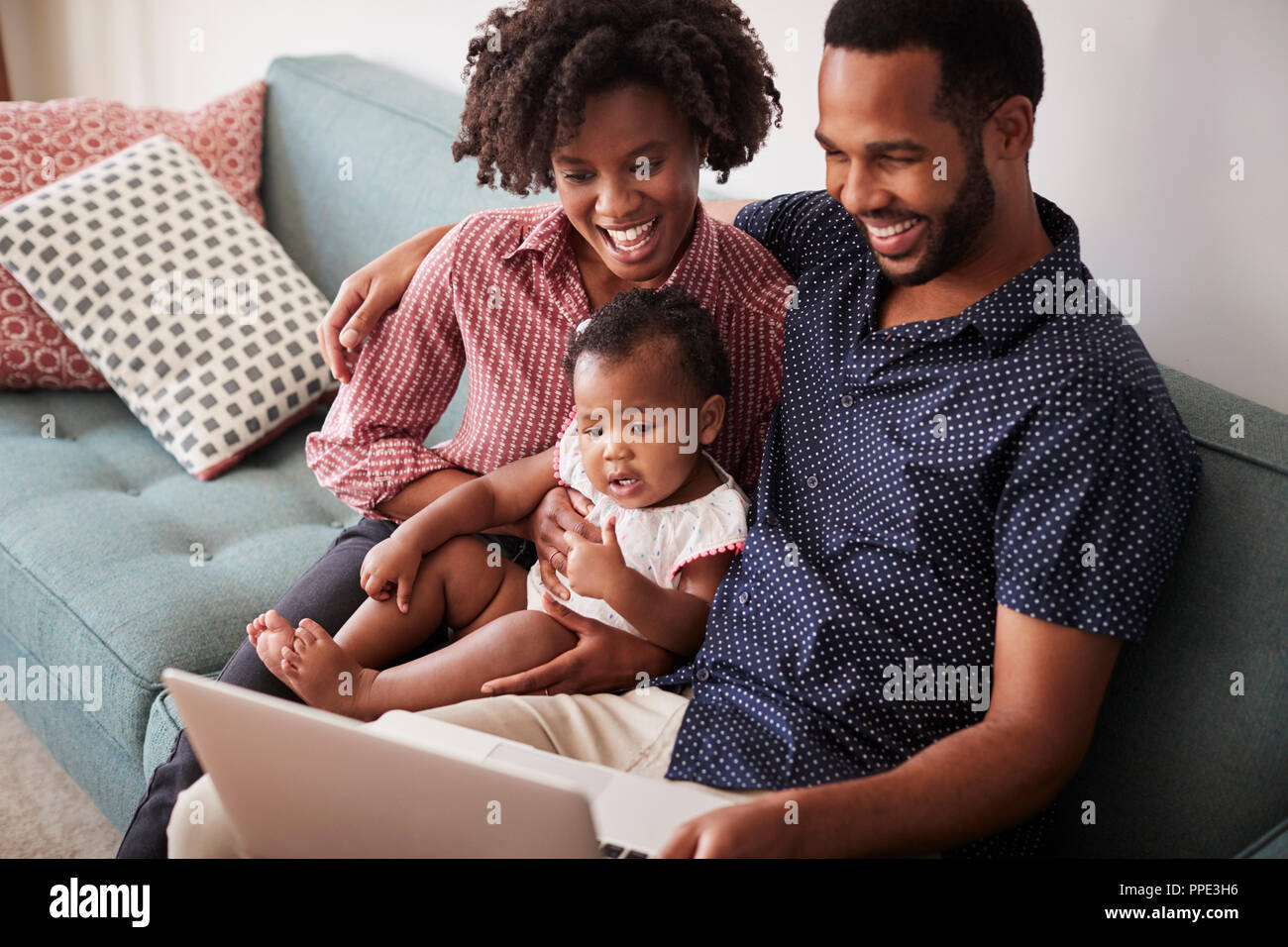 Familie mit Baby Tochter sitzt auf einem Sofa zu Hause auf Laptop Stockfoto