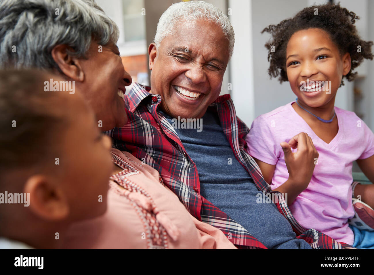 Großeltern entspannt auf einem Sofa zu Hause mit Enkelinnen Stockfoto