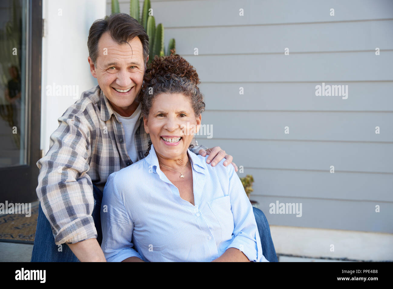 Portrait von Senior Paar außerhalb Graue Schindeln Haus sitzt Stockfoto