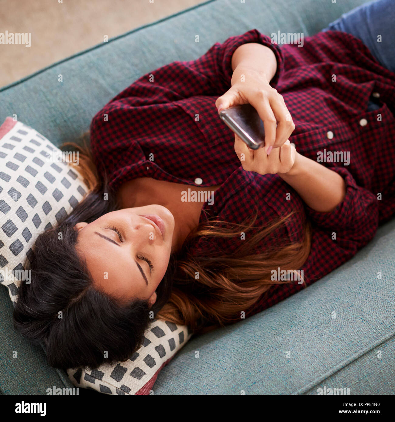 Ansicht der Frau liegend auf dem Sofa zu Hause mit Handy Stockfoto