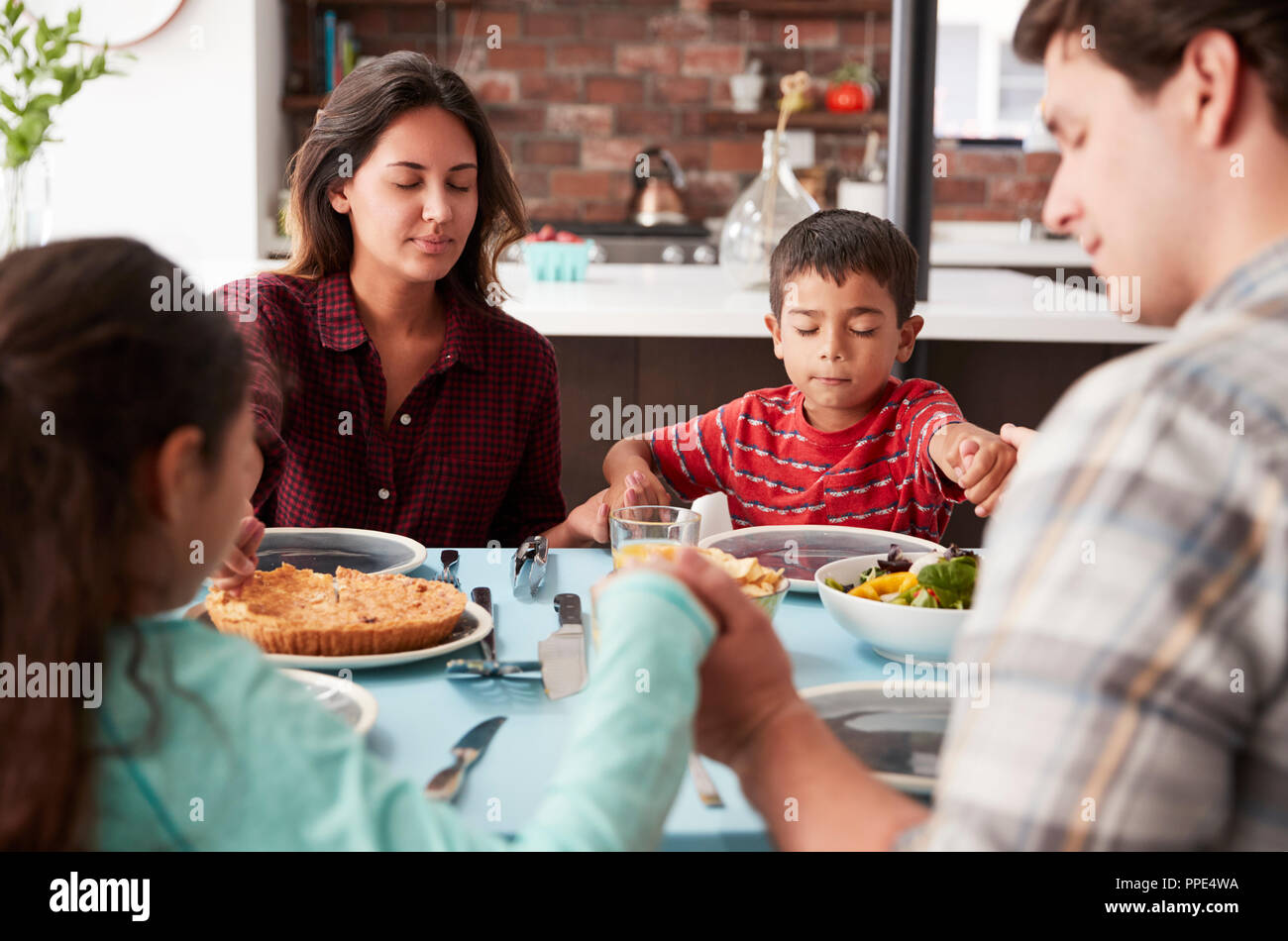 Familie Beten vor dem Essen um den Tisch zu Hause. Stockfoto
