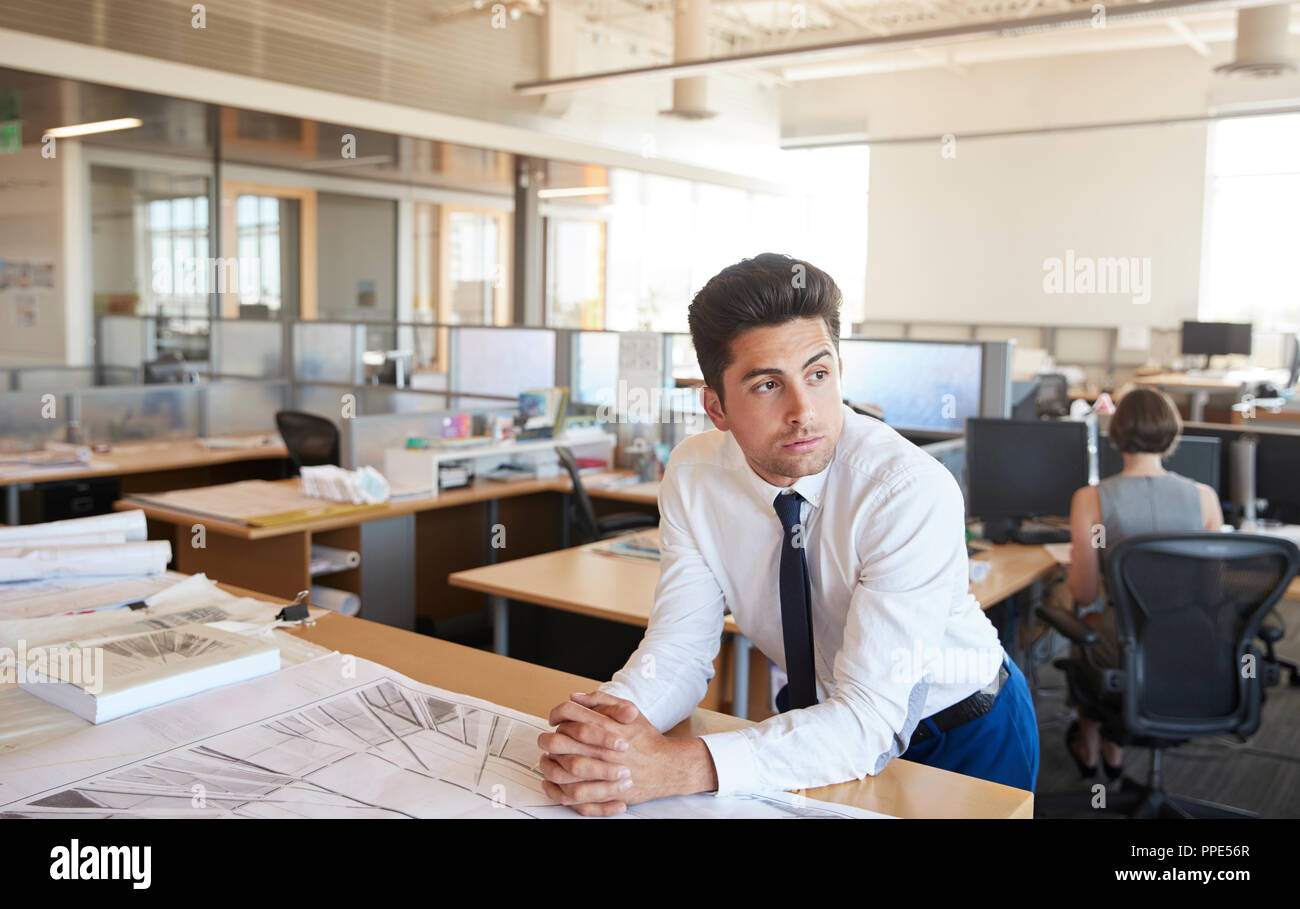 Junge männliche Architekt lehnte sich auf Schreibtisch im Großraumbüro Stockfoto